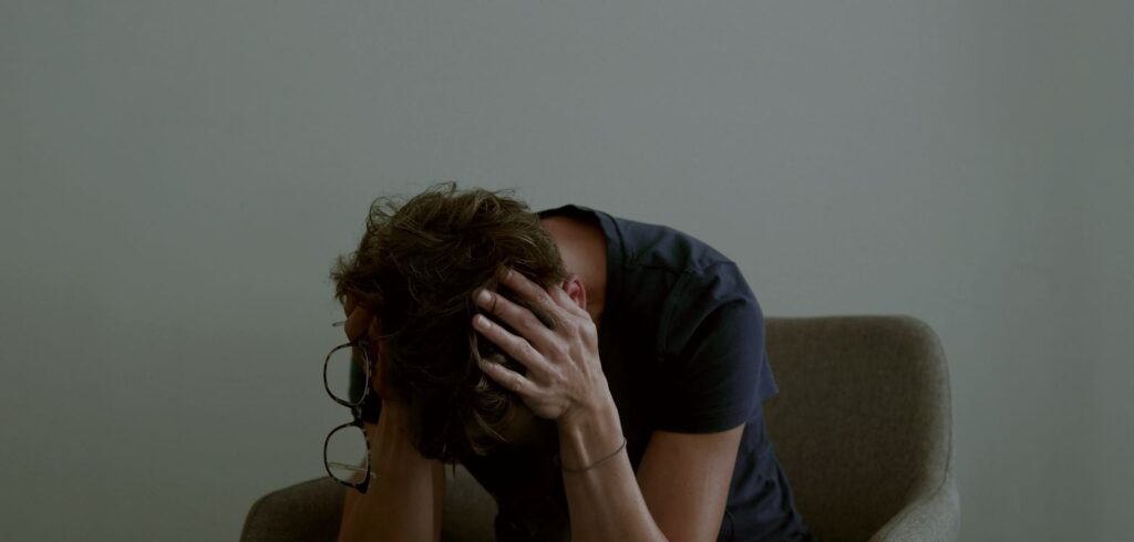 Vrouw met handen over haar oren. Zit voorover gebogen.